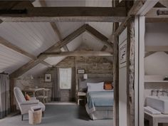 an attic bedroom with stone walls and exposed ceiling, white bedding, two armchairs and a large tub in the corner