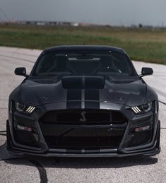 the front end of a black sports car on a track with grass in the background