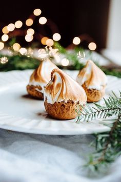 three desserts are sitting on a white plate with greenery and lights in the background