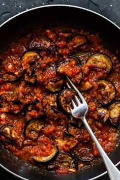 an iron skillet with cooked eggplant and tomato sauce on the side next to a fork