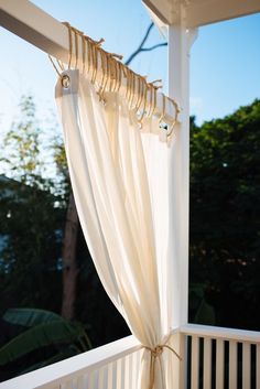 an open curtain on the outside of a white porch with trees in the back ground