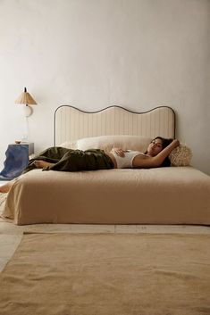 a woman laying on top of a bed next to a nightstand and lamp in a room