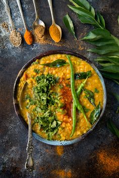 a bowl filled with food next to spoons and green beans on top of a table