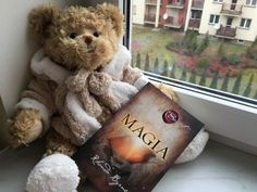 a teddy bear sitting next to a book on a window sill