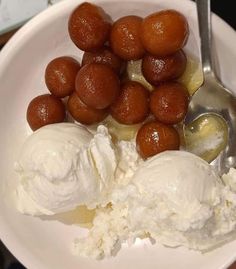 a white plate topped with ice cream and balls of fruit next to a spoon on top of a table