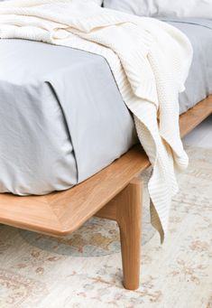 a bed with a blanket on top of it next to a wooden foot board and rug