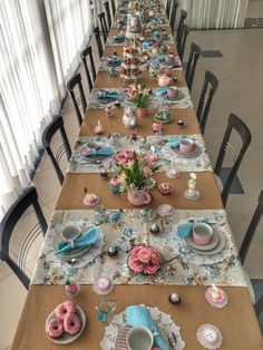 a long table is set with pink and blue plates, cups, and saucers