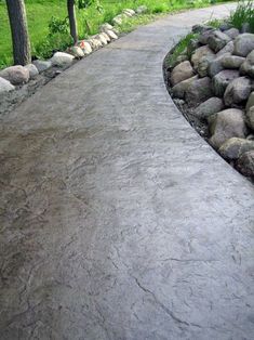 a stone path in the middle of a grassy area with trees and rocks on either side