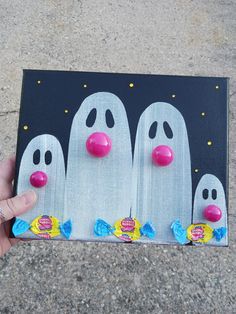 a hand holding up a piece of art with three ghost faces on it and candy candies in front of them