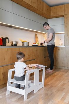 a young boy sitting at a small table in front of a man standing over it