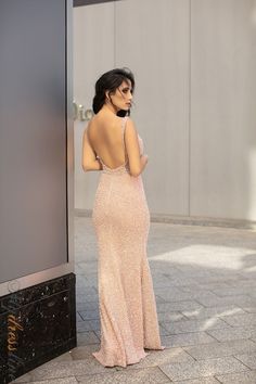 a woman in a long pink dress leaning against a wall looking at her cell phone