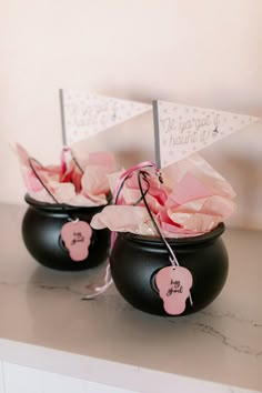 two black vases with pink flowers in them on top of a white countertop