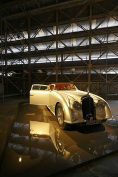 an antique car is on display in front of a large metal structure with lights shining from it