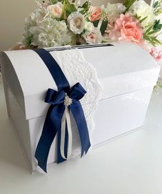 a white box with blue ribbon and flowers in the background