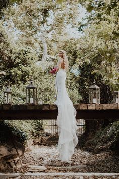 a woman in a white wedding dress standing on a bridge with trees and lanterns behind her