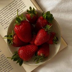 strawberries in a bowl on top of an open book