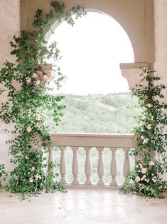 an archway with flowers and greenery on the side of a white wall next to a balcony