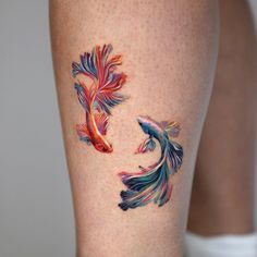 two goldfish tattoos on the legs of a woman's leg, both with different colors