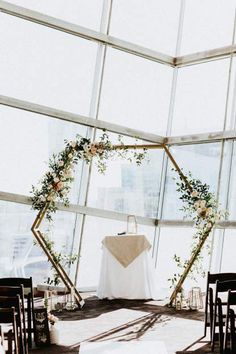 a wedding ceremony setup with white linens and greenery in front of a large window