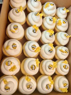 a box filled with lots of cupcakes covered in white frosting and yellow decorations