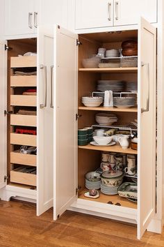 an open cabinet filled with lots of dishes on top of a wooden floor next to white cabinets