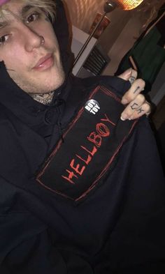 a young man wearing a black hoodie with the word hell written on it, holding up a t - shirt