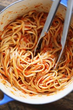 spaghetti being cooked in a pot with tongs