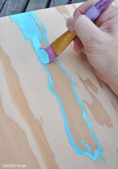 a person is painting on wood with blue and yellow paint while holding a purple crayon