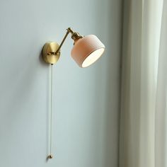 a wall mounted light on the side of a white wall next to a window with curtains