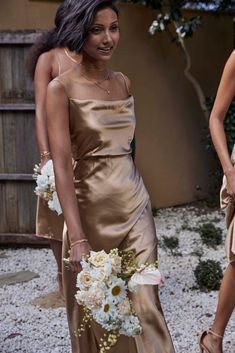 two women in gold dresses standing next to each other holding bouquets and smiling at the camera