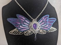 This gorgeous necklace features purple, black, and silver fairy wings with a opalescent purple gem in the middle. A drop crystal hangs from the center. Perfect for special occasions or to add a bit of magic to your everyday! Handmade Purple Fantasy Necklaces, Handmade Purple Fantasy Necklace, Purple Fantasy Necklace For Gift, Fantasy Style Purple Necklace For Gift, Purple Butterfly Charm Jewelry For Party, Magical Purple Pendant Necklace, Faerie Wedding, Magical Aesthetic, Silver Fairy