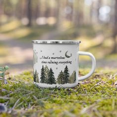 a white coffee mug sitting on top of a green grass covered forest floor next to a small plant