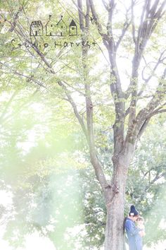 a man and woman standing next to a tree in the sun with their arms around each other