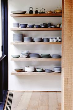 the shelves are filled with plates and bowls on wooden shelves in front of an open door