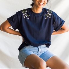 Boxy Fit Cotton Tee With A Crew Neck And Embroidered Daisies To The Shoulders. Blue Crew Neck Tops With Floral Embroidery, Blue Crew Neck Top With Floral Embroidery, Relaxed Fit Crew Neck Tops With Floral Embroidery, Relaxed Fit Floral Embroidery Tops With Crew Neck, Relaxed Fit Floral Embroidered Crew Neck Tops, Blue Floral Embroidered Crew Neck Top, Casual Black Top With Embroidered Hem, Blue Tops With Embroidered Text For Spring, Casual Crew Neck Tops With Embroidery