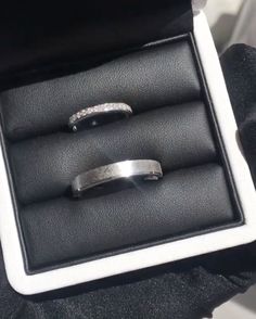 two wedding bands are in a box with black leather and white stitching on them