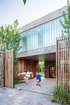 two young boys playing soccer in front of a modern building with wooden slats on the walls