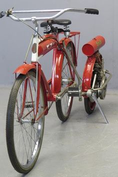 an old fashioned red bicycle is parked in a room with gray walls and flooring