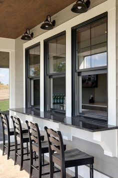 an outdoor bar with chairs and bottles on the outside wall, next to two windows