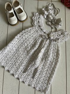 a crocheted dress and shoes are on the floor next to a pair of baby shoes