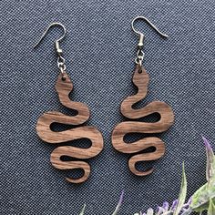 These laser cut snake earrings are made from your preference of 1/8" Maple or 1/8” Walnut hardwood. They’re light as a feather and ideal for daily wear! Choose either gold tone or silver tone hardware. Ear wires are stainless steel. Wood part of earring measures approximately 2” tall and 1.16” wide. Laser cut, crafted by hand and shipped from the United States. Wood grain varies with every piece and computer monitor settings can vary which may result in displaying slight color differences. You s Laser Cut Keychains, Basswood Projects, Laser Cut Earrings Wood, Wood Snake, Laser Cut Wood Jewelry, Snake Wood, Wood Jewelery, Laser Cut Wood Earrings, Engraving Ideas