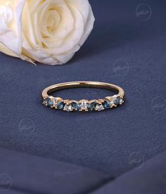 an image of a wedding ring with blue stones on it and a rose in the background