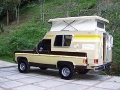 an old truck with a camper attached to it's bed is parked in front of a grassy hill