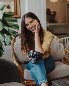 a woman sitting on top of a couch holding a camera next to her face and smiling