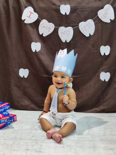 a baby sitting on the floor wearing a birthday hat