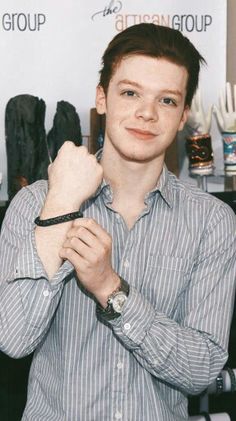 a young man is posing for the camera with his watch around his neck and wearing a striped shirt