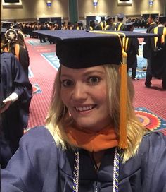 a woman wearing a graduation cap and gown in a room full of people with other graduates