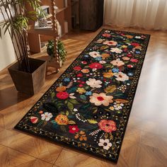 a black rug with colorful flowers on it in front of a wooden floor and potted plant