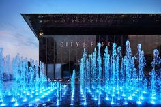 the city park is lit up with blue lights and water spouting from it