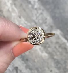 a woman's hand holding a yellow gold ring with a diamond in the center